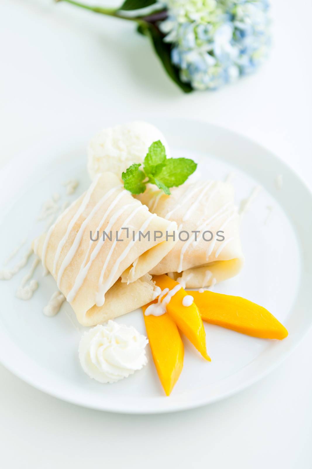 Thai style tropical dessert crepes filled with fresh mango sticky rice and a scoop of coconut ice cream. Shallow depth of field.