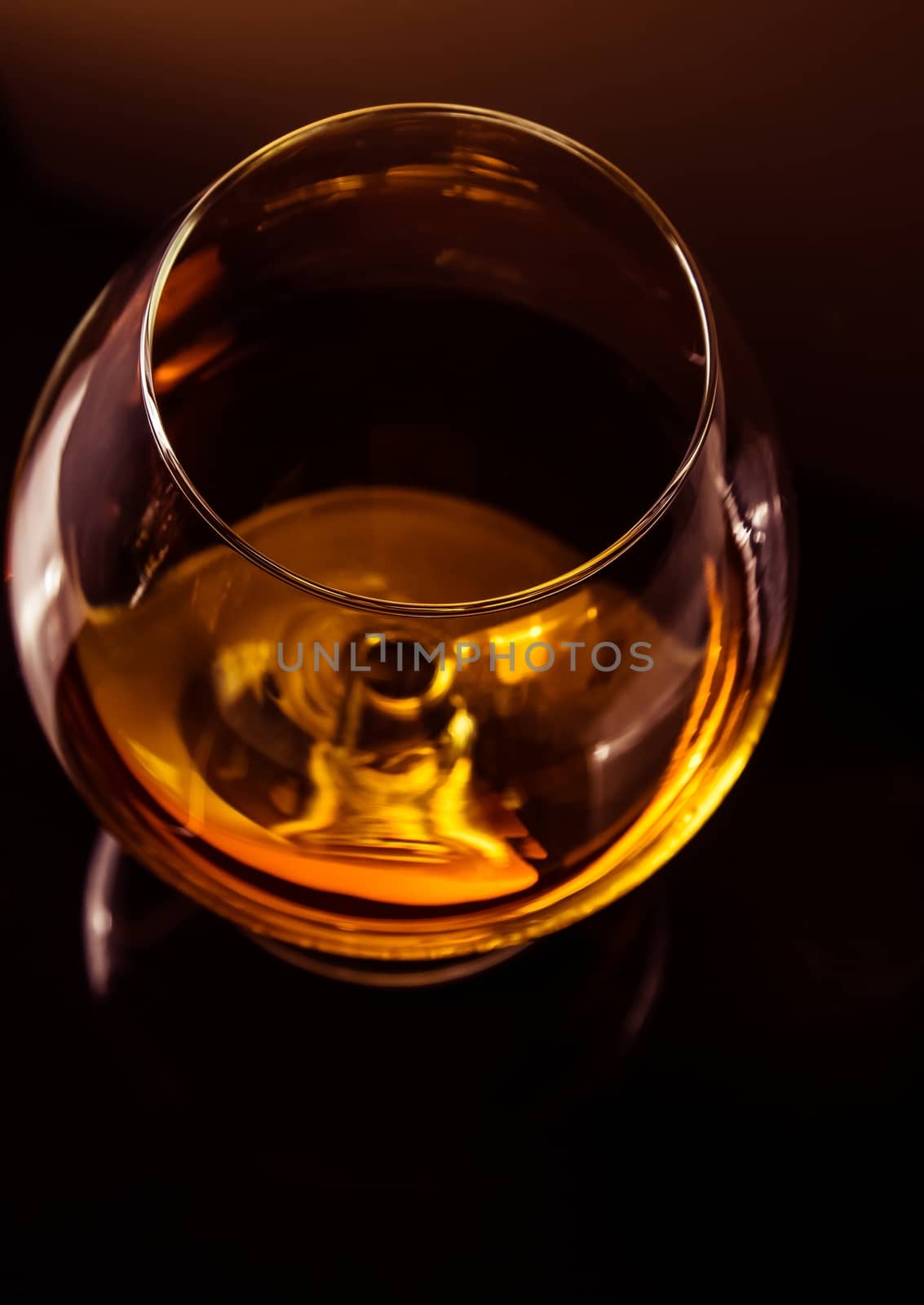 top of view of snifter of brandy in elegant typical cognac glass on dark background with golden reflection, warm atmosphere