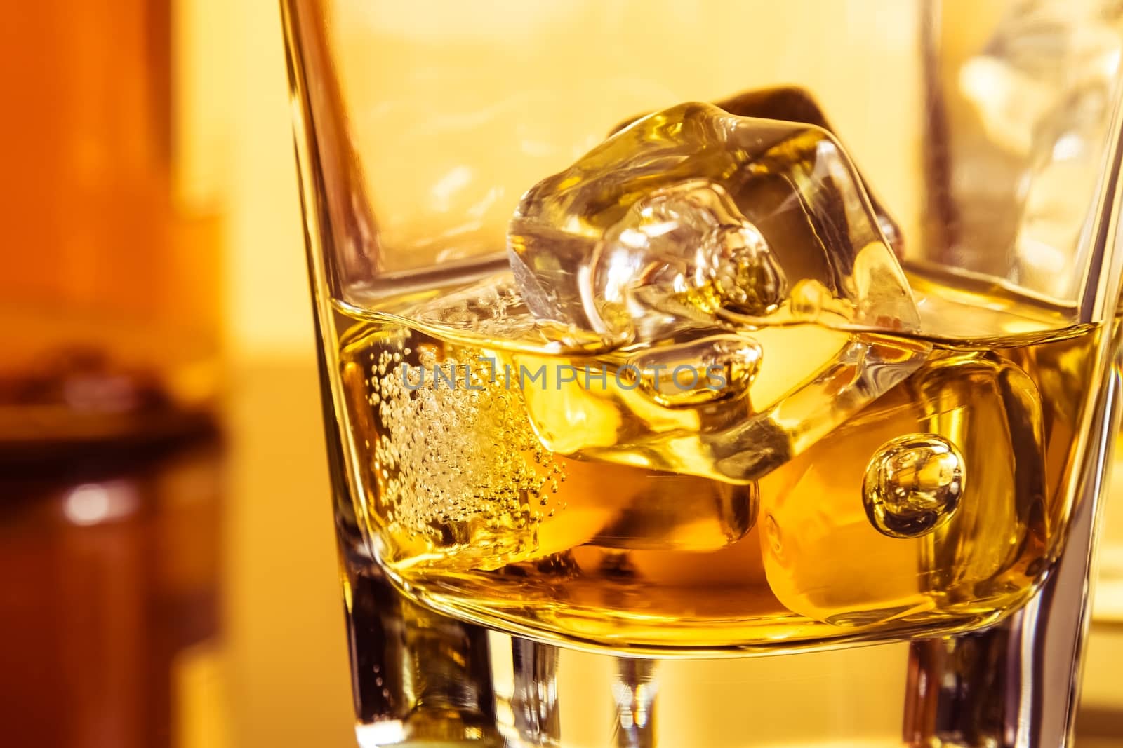 detail of glass of whiskey with ices near bottle on table with reflection, warm atmosphere, time of relax with whisky