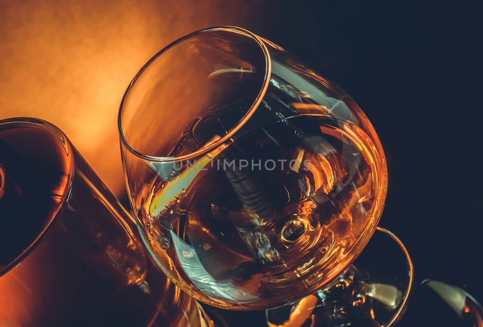 snifter of brandy in elegant typical cognac glass near bottle on black table warm tint style with space for text