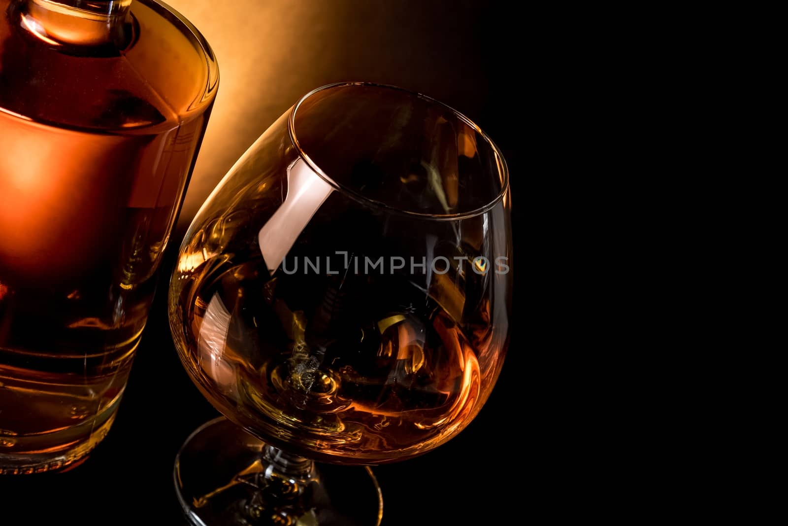 snifter of brandy in elegant typical cognac glass near bottle on black table with space for text