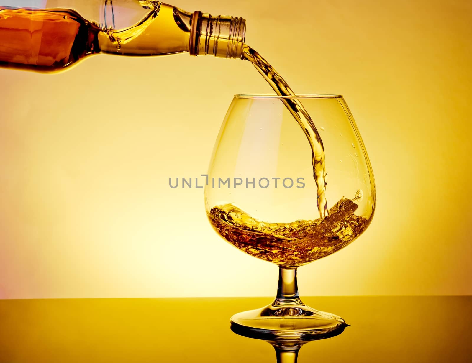 barman pouring snifter of brandy in elegant typical cognac glass on table on warm atmosphere