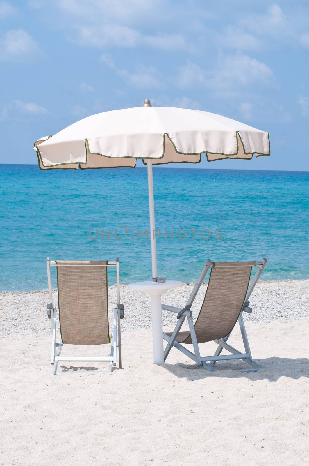 two deckchairs on the beach under an umbrella