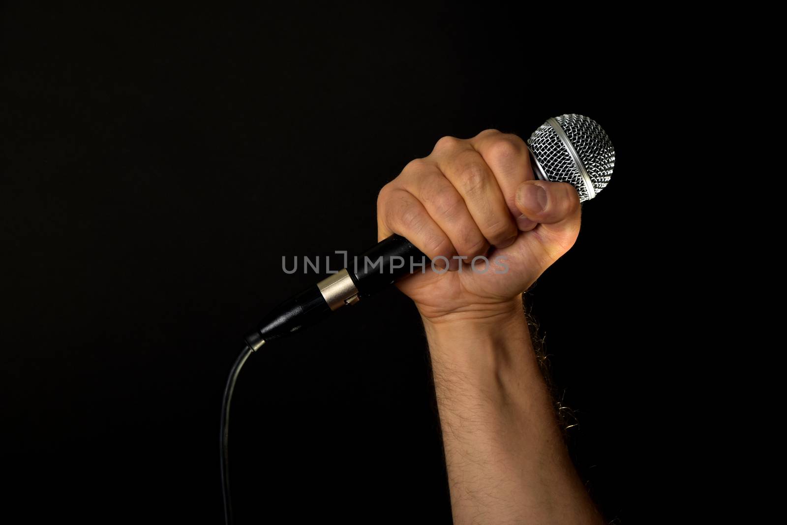 Male hand holding microphone with wire cable isolated on black background