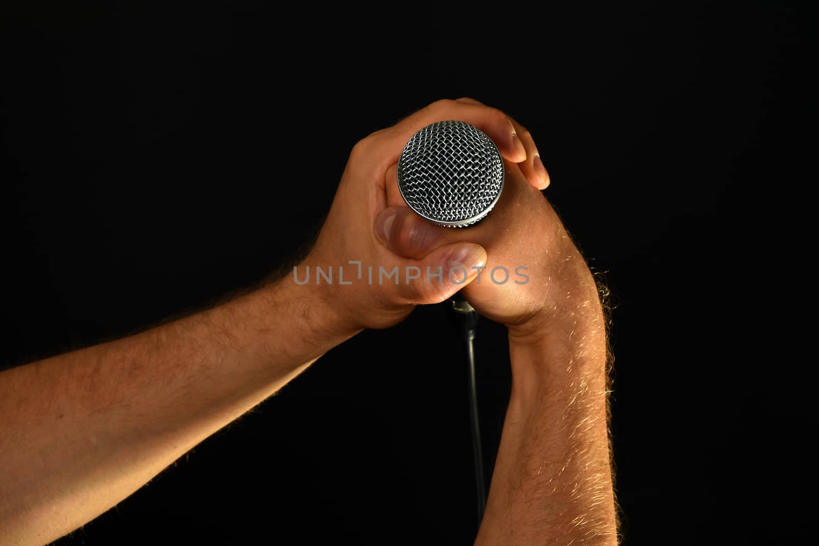 Two male hands holding microphone with wire cable isolated on black background