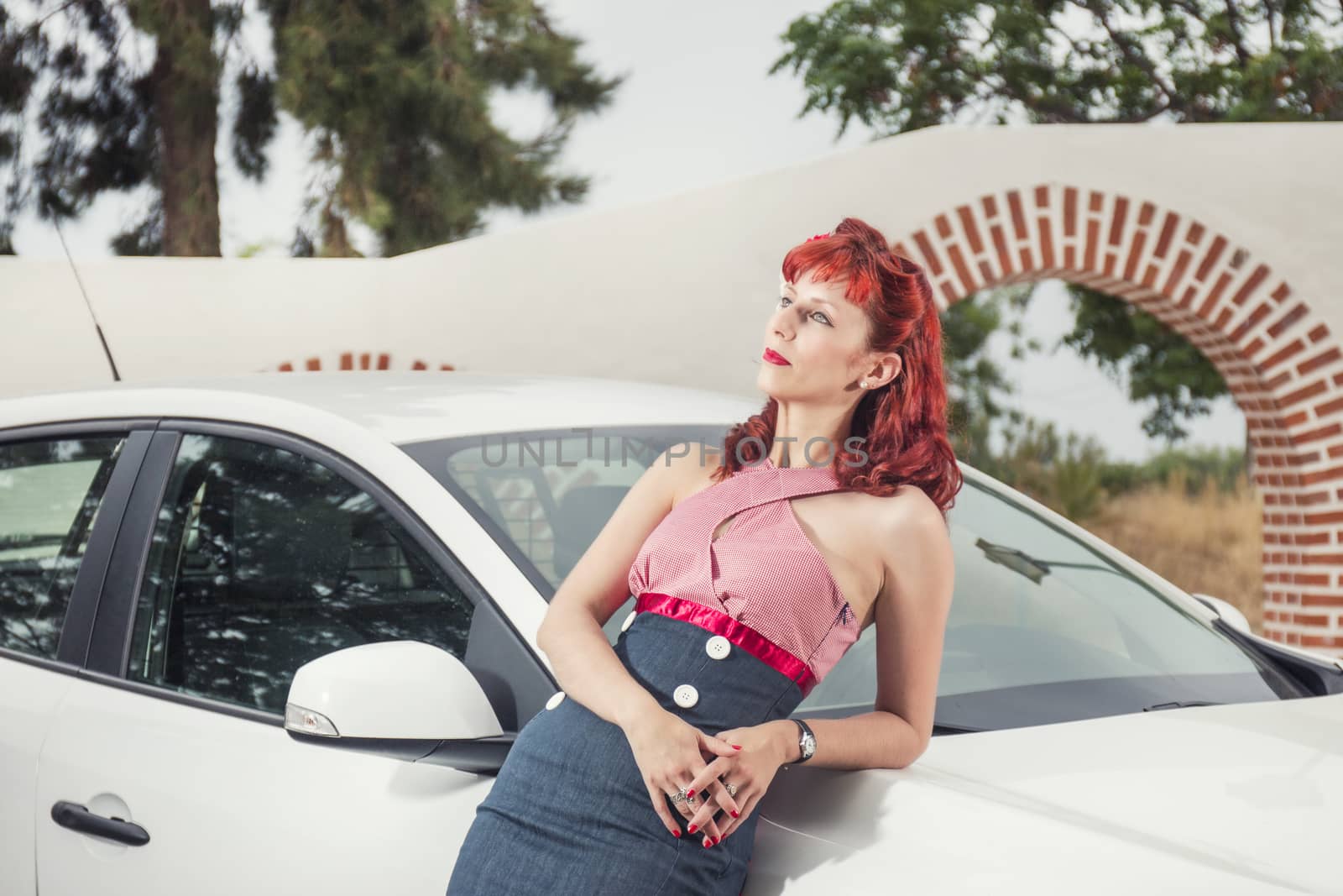 View of pinup young woman in vintage style clothing next to a white car.