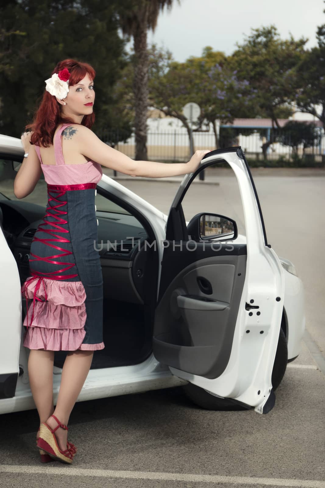 View of pinup young woman in vintage style clothing next to a white car.