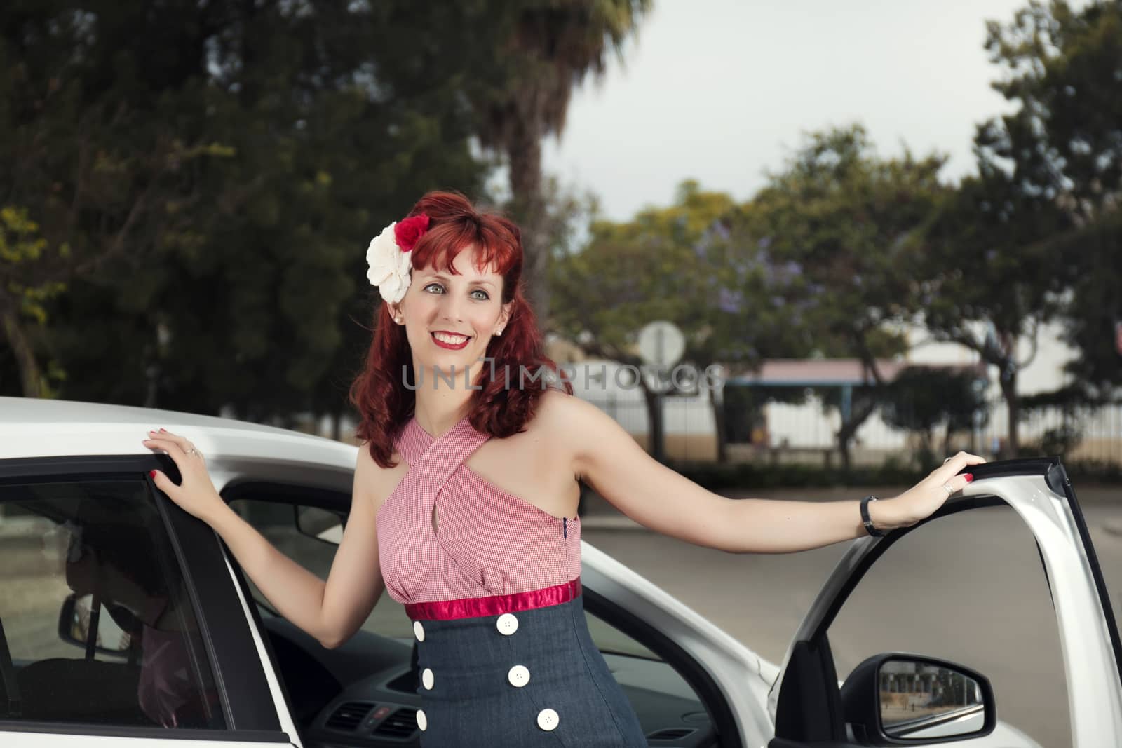 View of pinup young woman in vintage style clothing next to a white car.