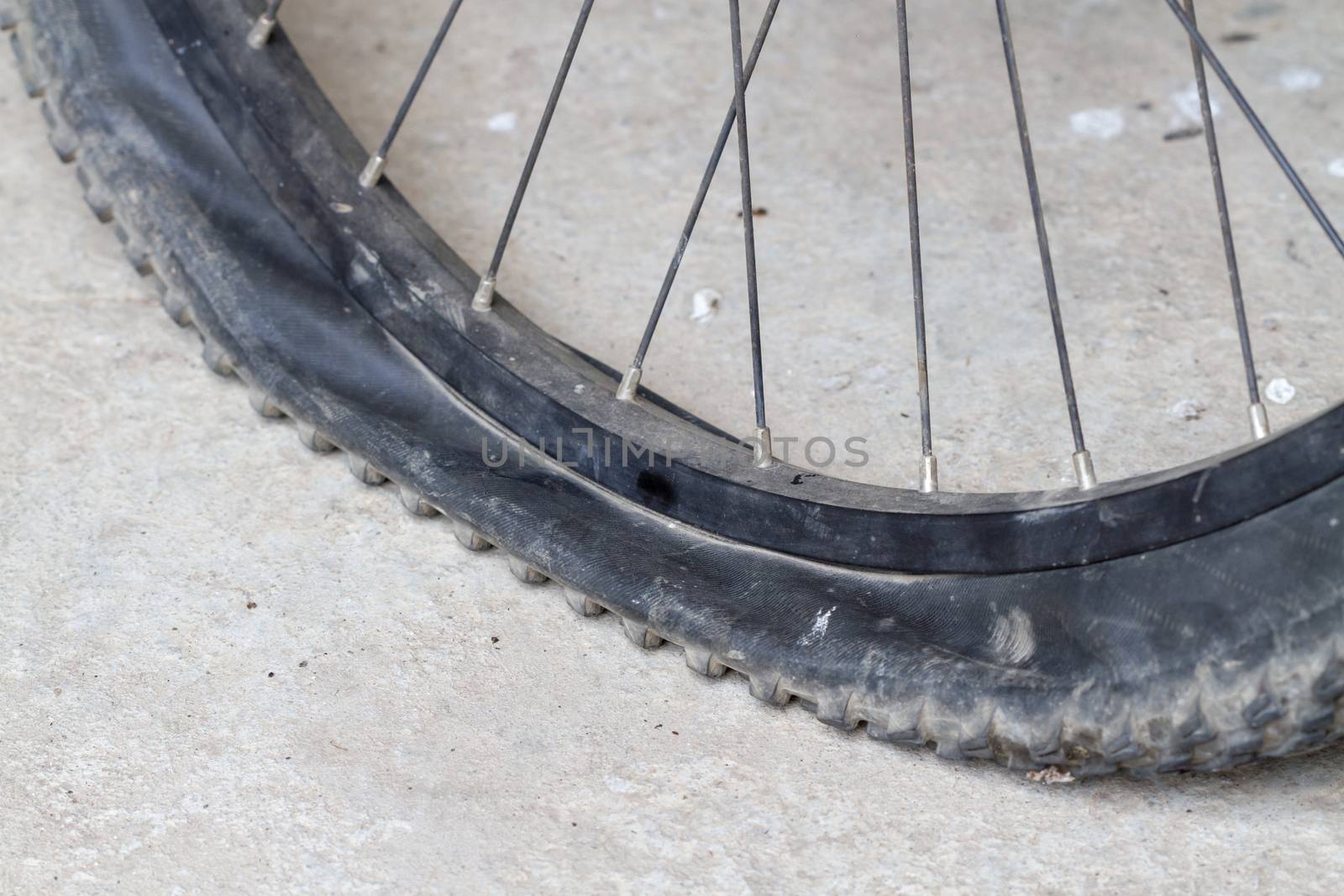 old Bicycle wheel with flat tyre on road by supersaiyan