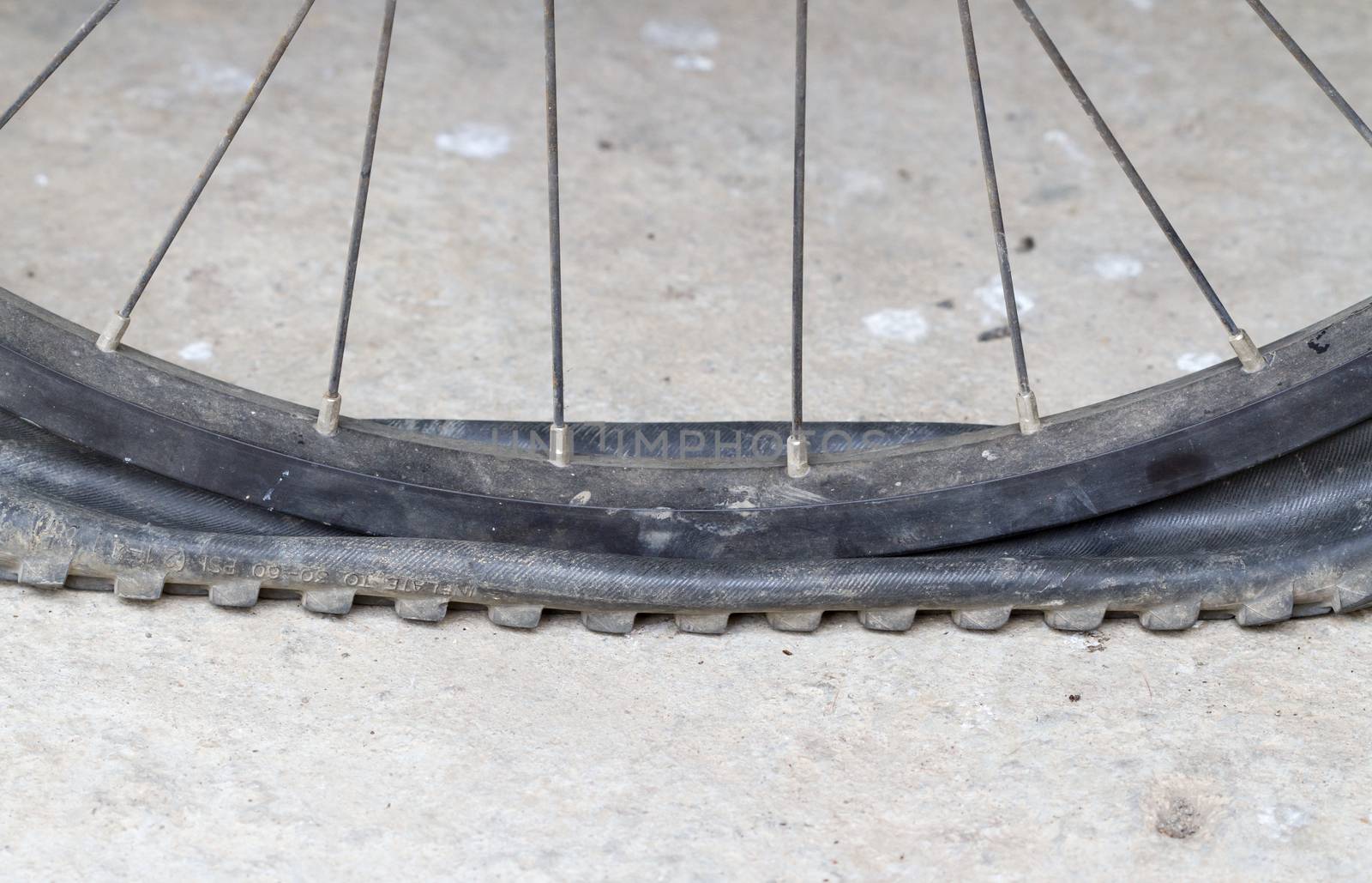 old Bicycle wheel with flat tyre on road by supersaiyan