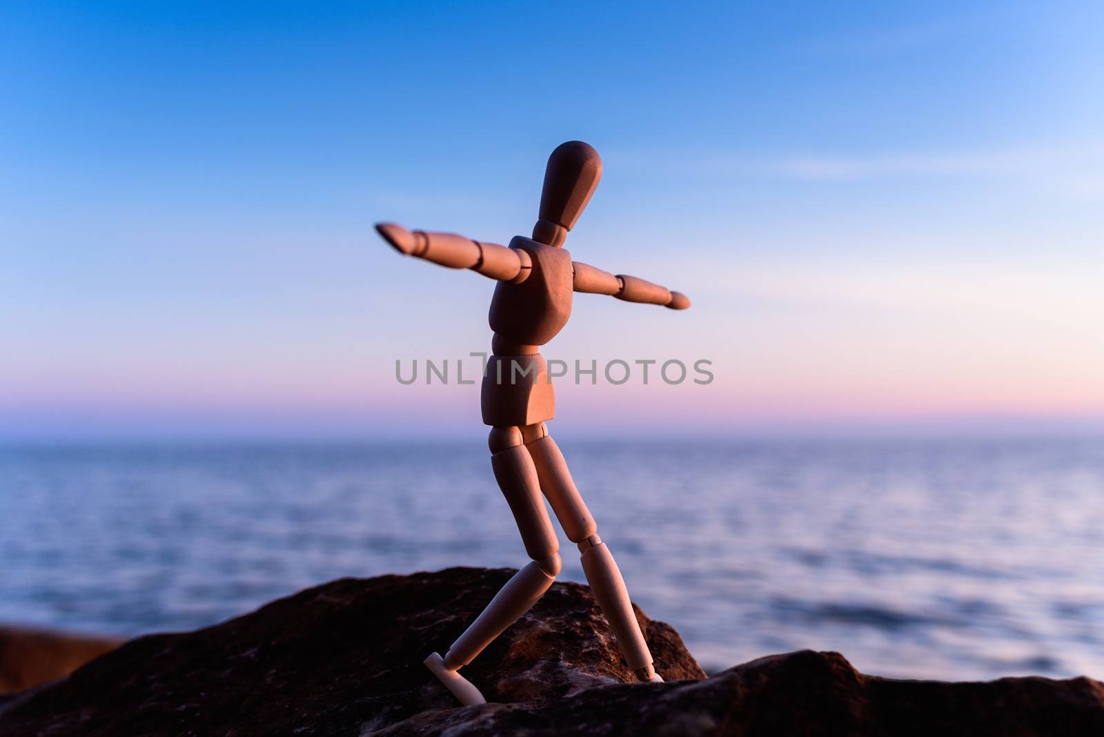 Wooden man stands on the top of sea boulder