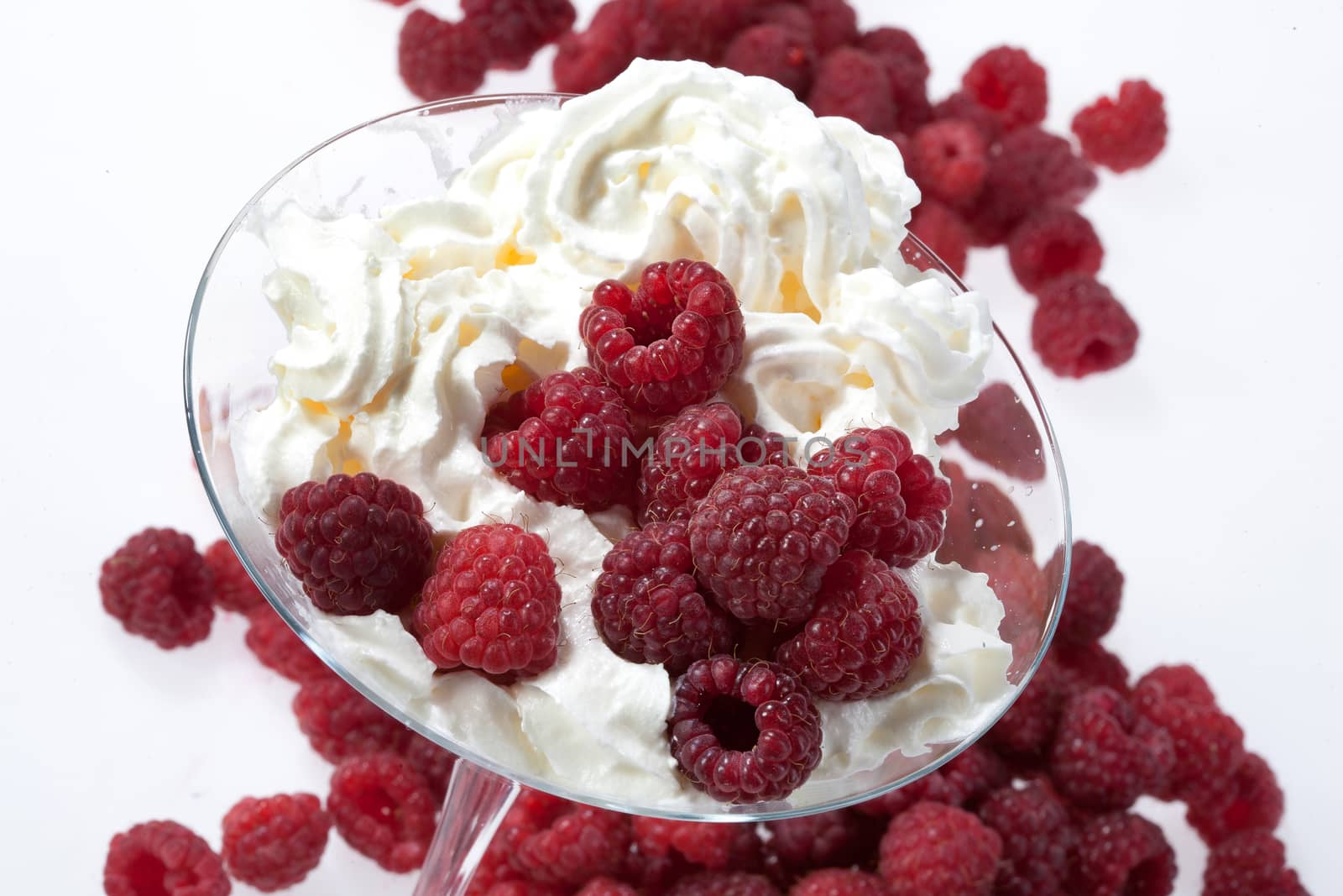 Glass with whipped cream and raspberries on a studio background