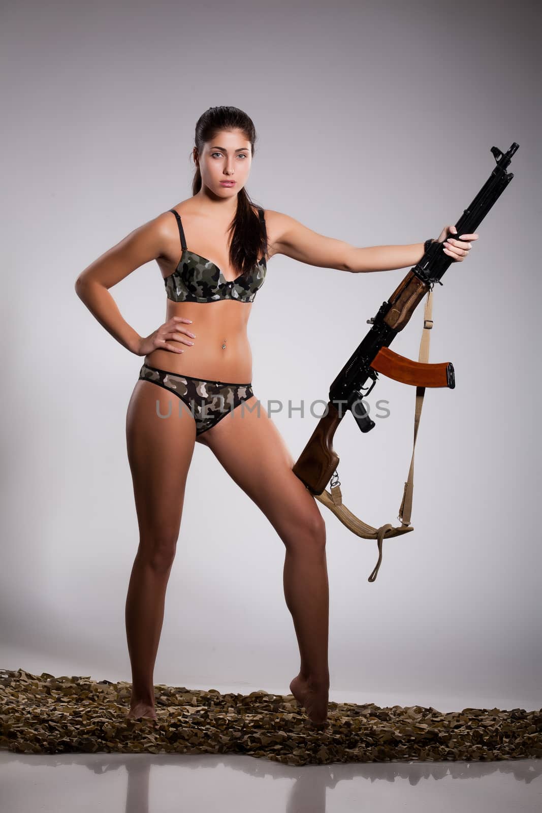 Young beautiful barefoot woman in camouflaged lingerie with light machinegun