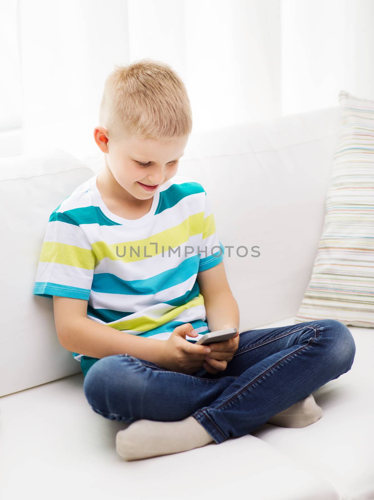 smiling little boy with smartphone at home by dolgachov