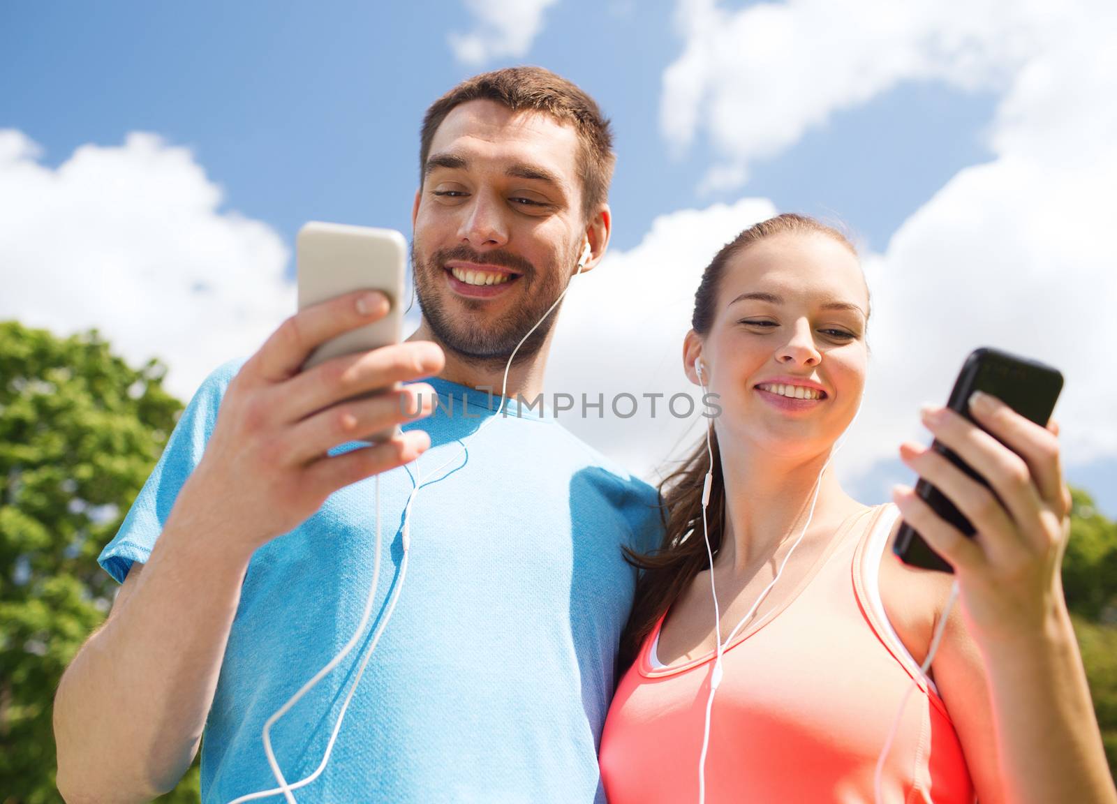 two smiling people with smartphones outdoors by dolgachov
