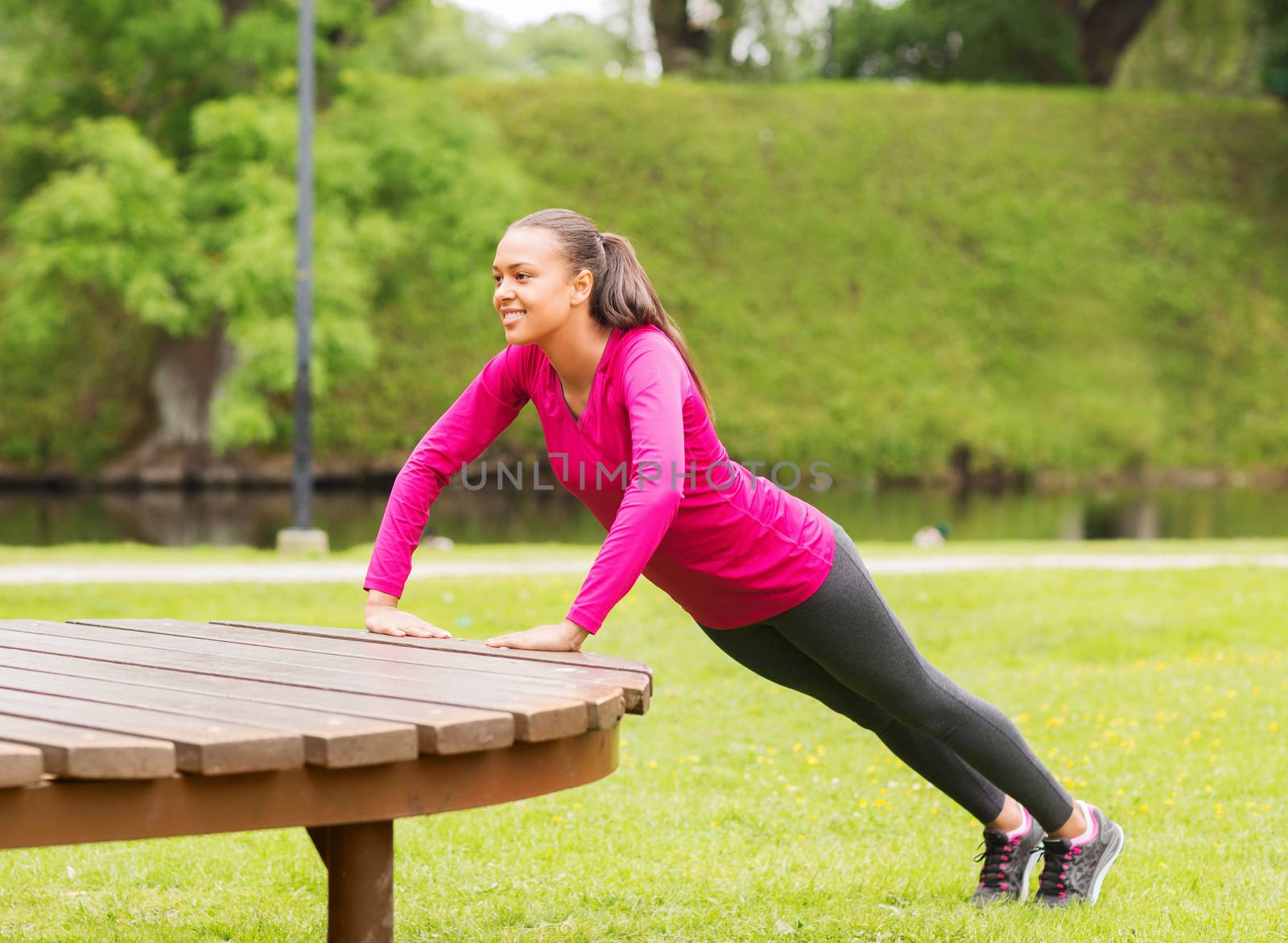 fitness, sport, training, park and lifestyle concept - smiling african american woman doing push-ups on bench outdoors