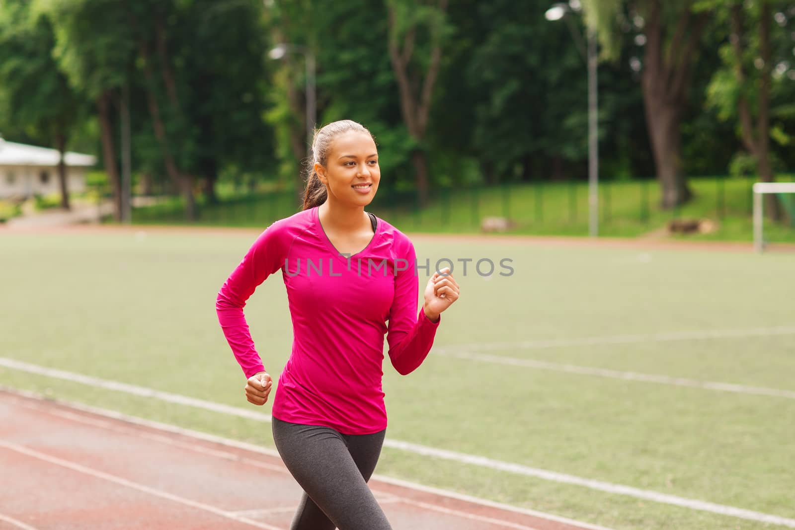 smiling woman running on track outdoors by dolgachov