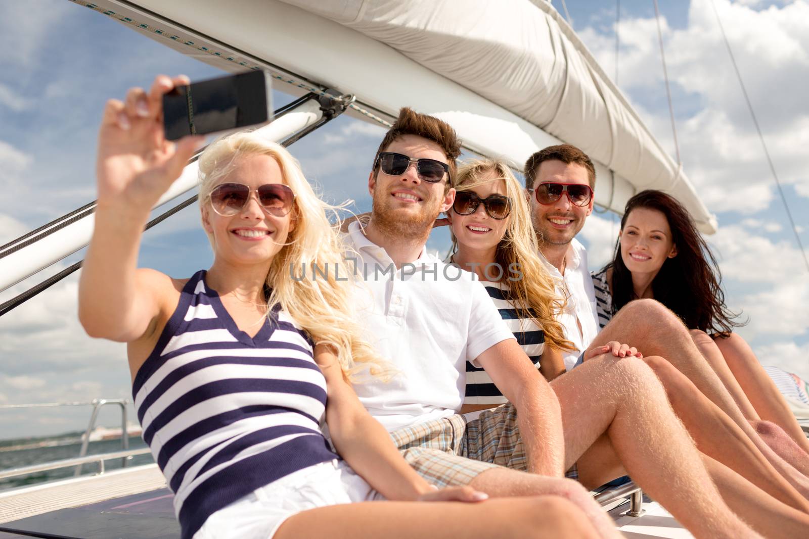 vacation, travel, sea, friendship and people concept - smiling friends sitting on yacht deck and making selfie