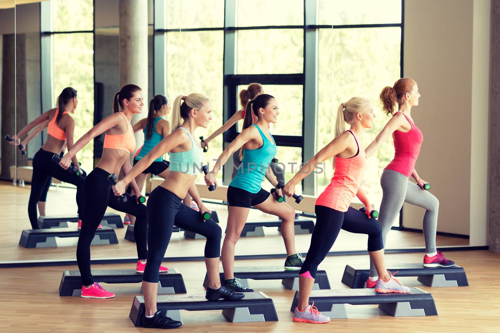 fitness, sport, training, gym and lifestyle concept - group of women working out with dumbbells and steppers in gym