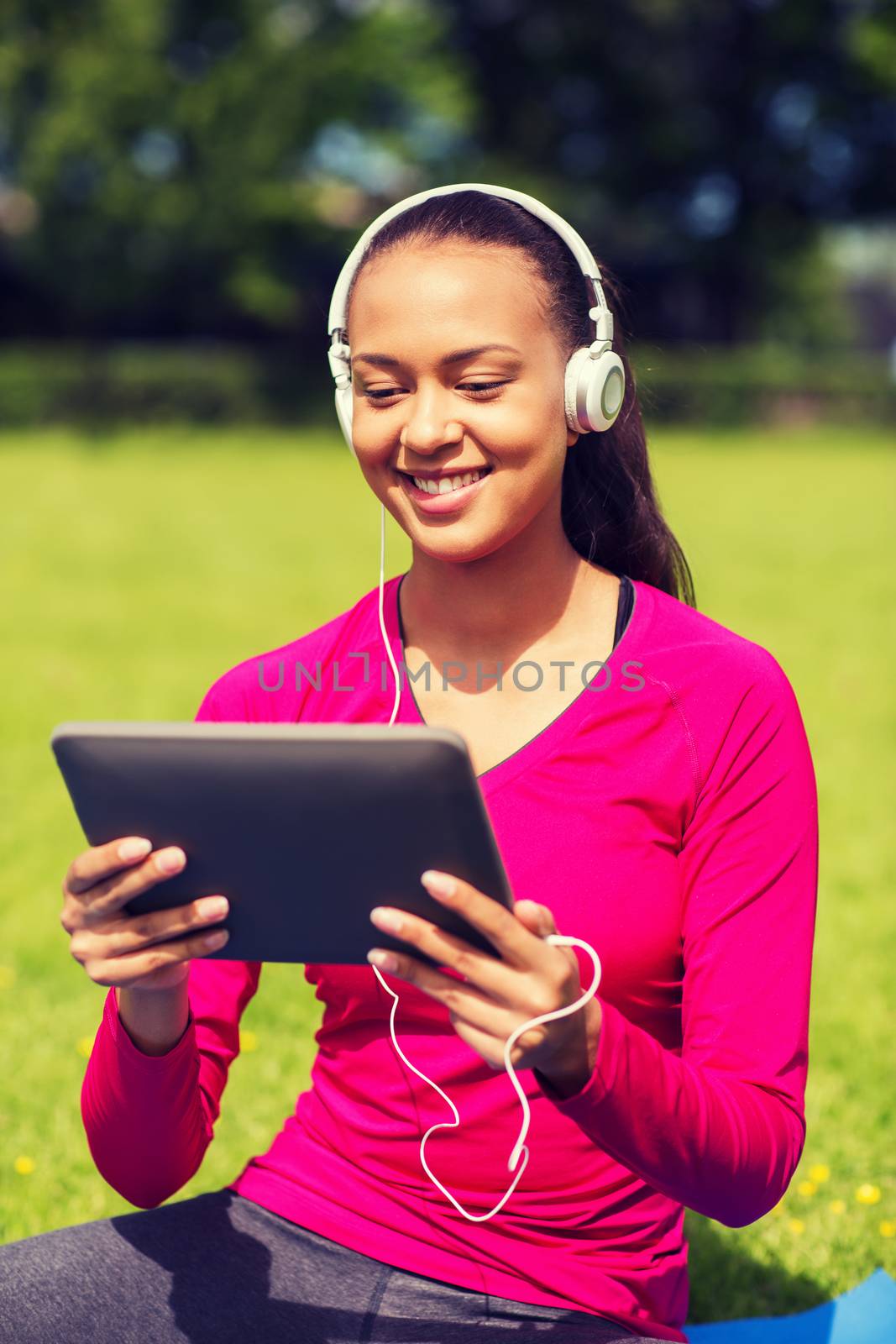 fitness, park, technology and sport concept - smiling african american woman with tablet pc computer and headphones on mat outdoors