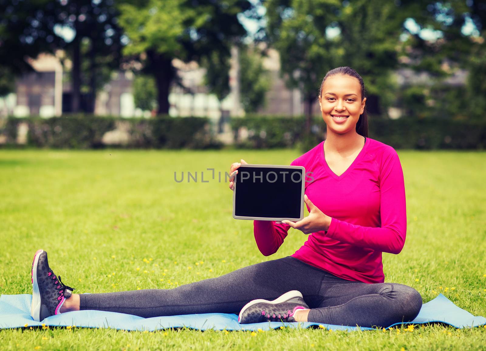 fitness, park, technology and sport concept - smiling african american woman with tablet pc computer sitting on mat outdoors