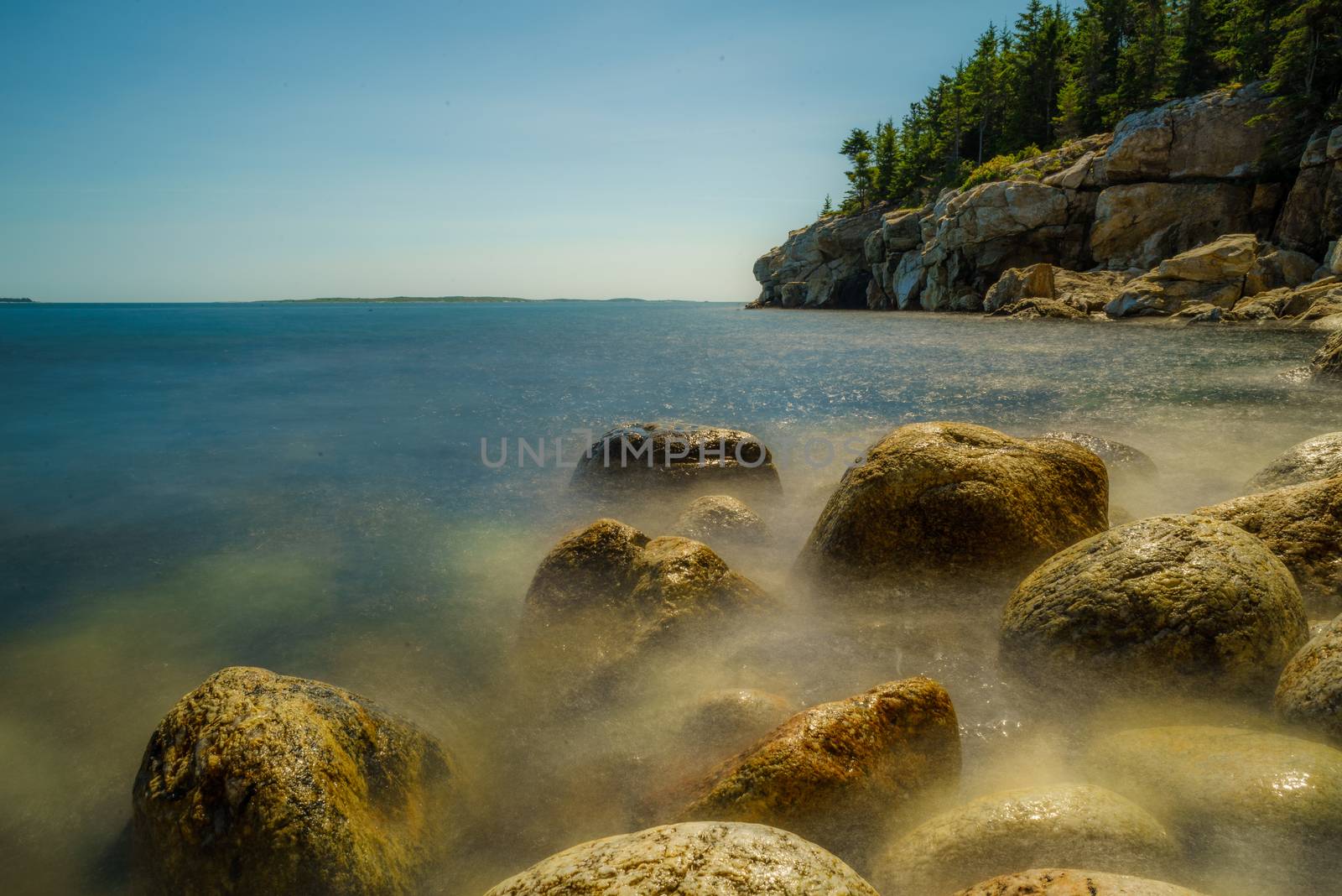 A time lapse picture of e soft, rock-strewn beach against a granite cliff in Maine
