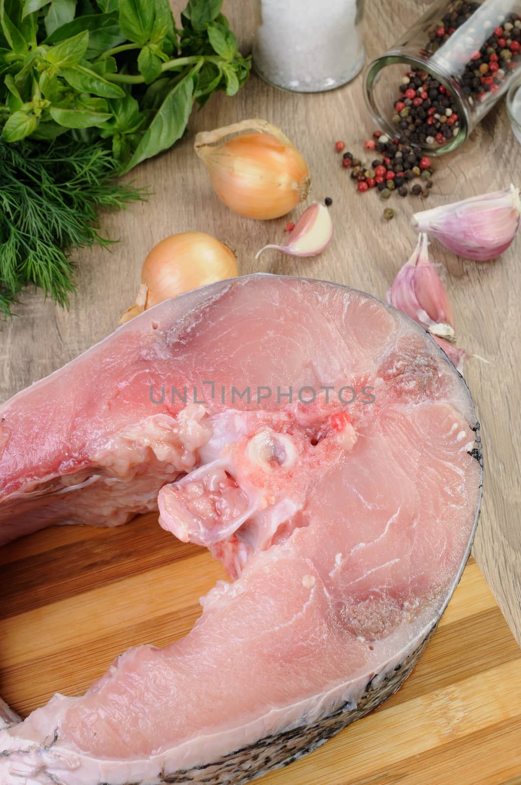 Raw piece (steak) carp on wooden board with fresh herbs and spices