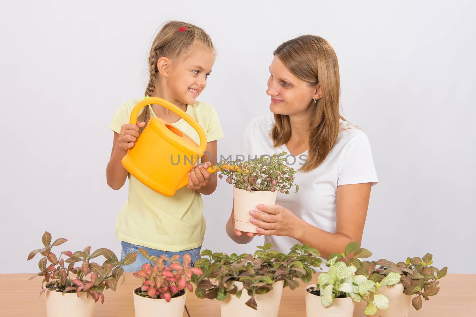 Happy mother and daughter looking at each other watering flowers by Madhourse