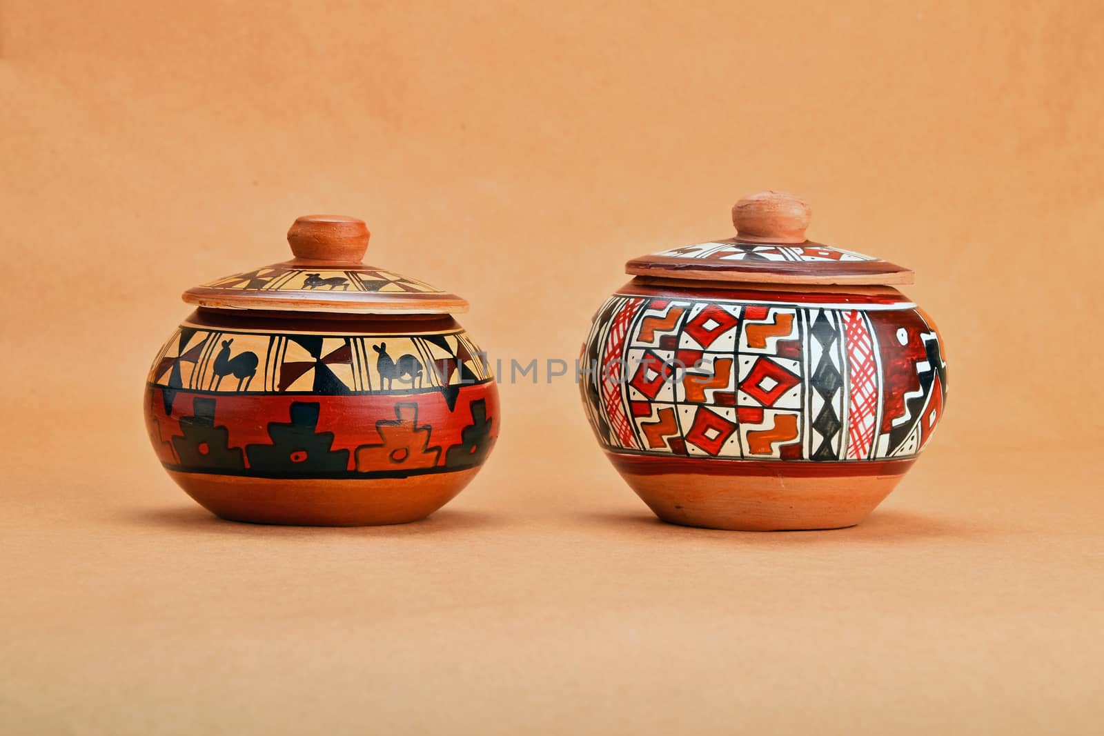Two painted handmade traditional Latin American ceramic pot with closed lid on kraft paper background