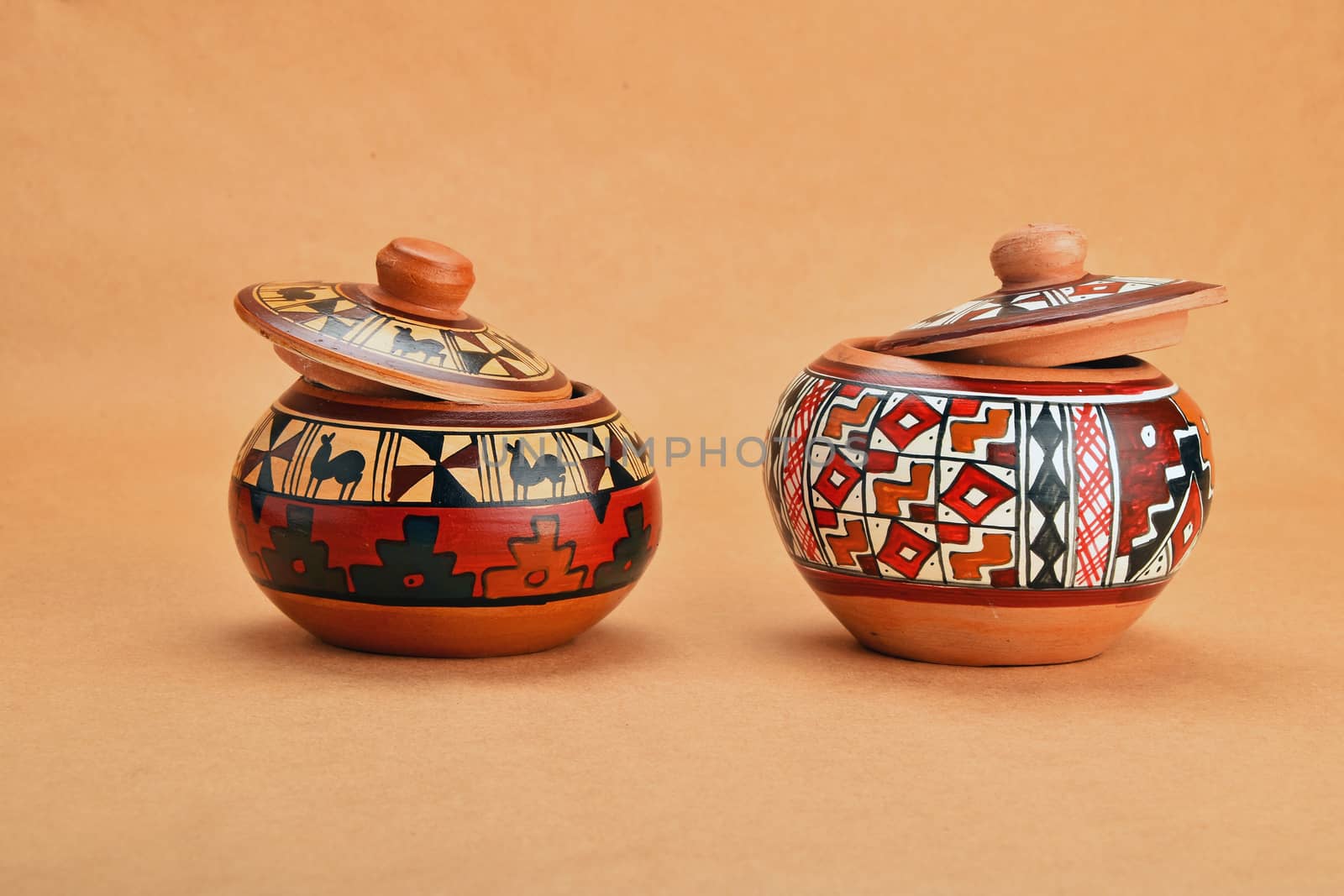 Two painted handmade traditional Latin American ceramic pot with closed lid on kraft paper background