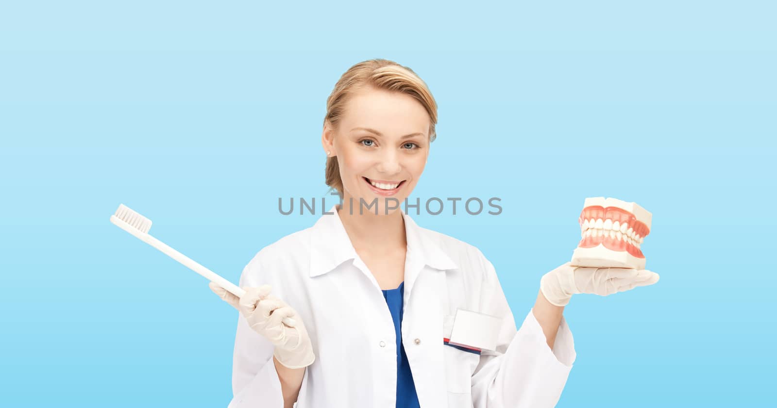 medicine, stomatology, people and hygiene concept - smiling female doctor holding toothbrush and jaws model over blue background