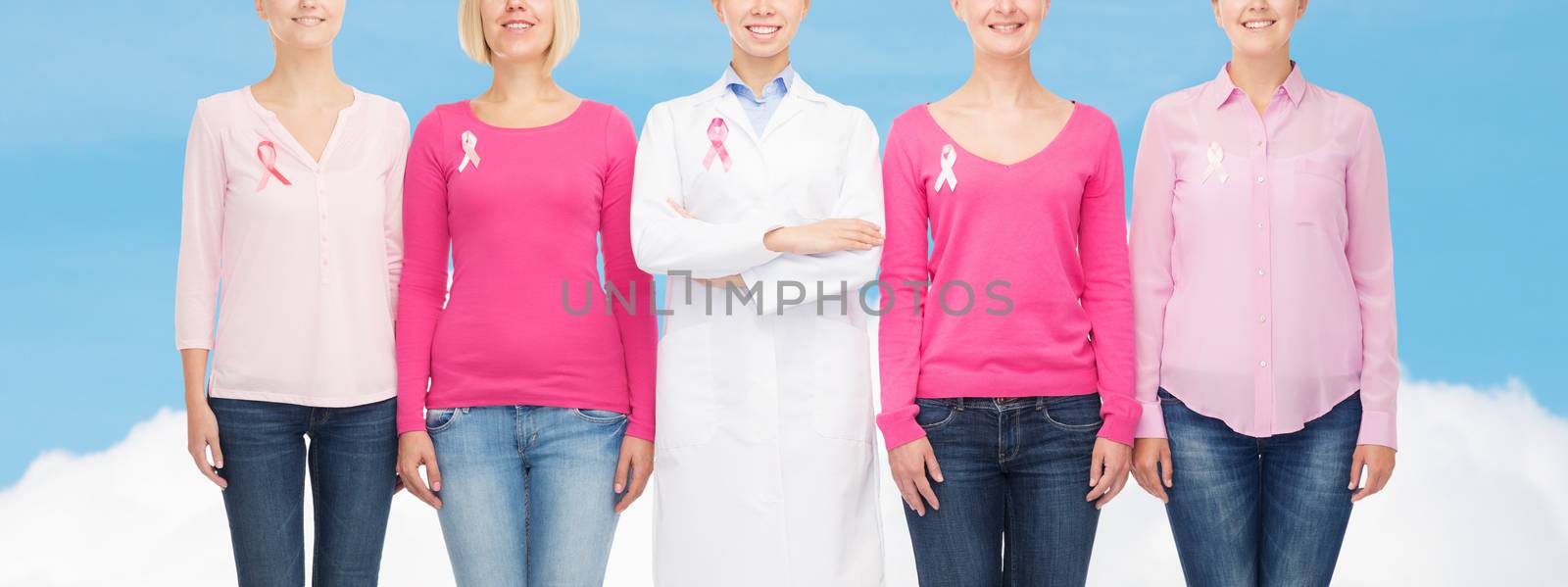 healthcare, people and medicine concept - close up of smiling women in blank shirts with pink breast cancer awareness ribbons over blue sky and white cloud background