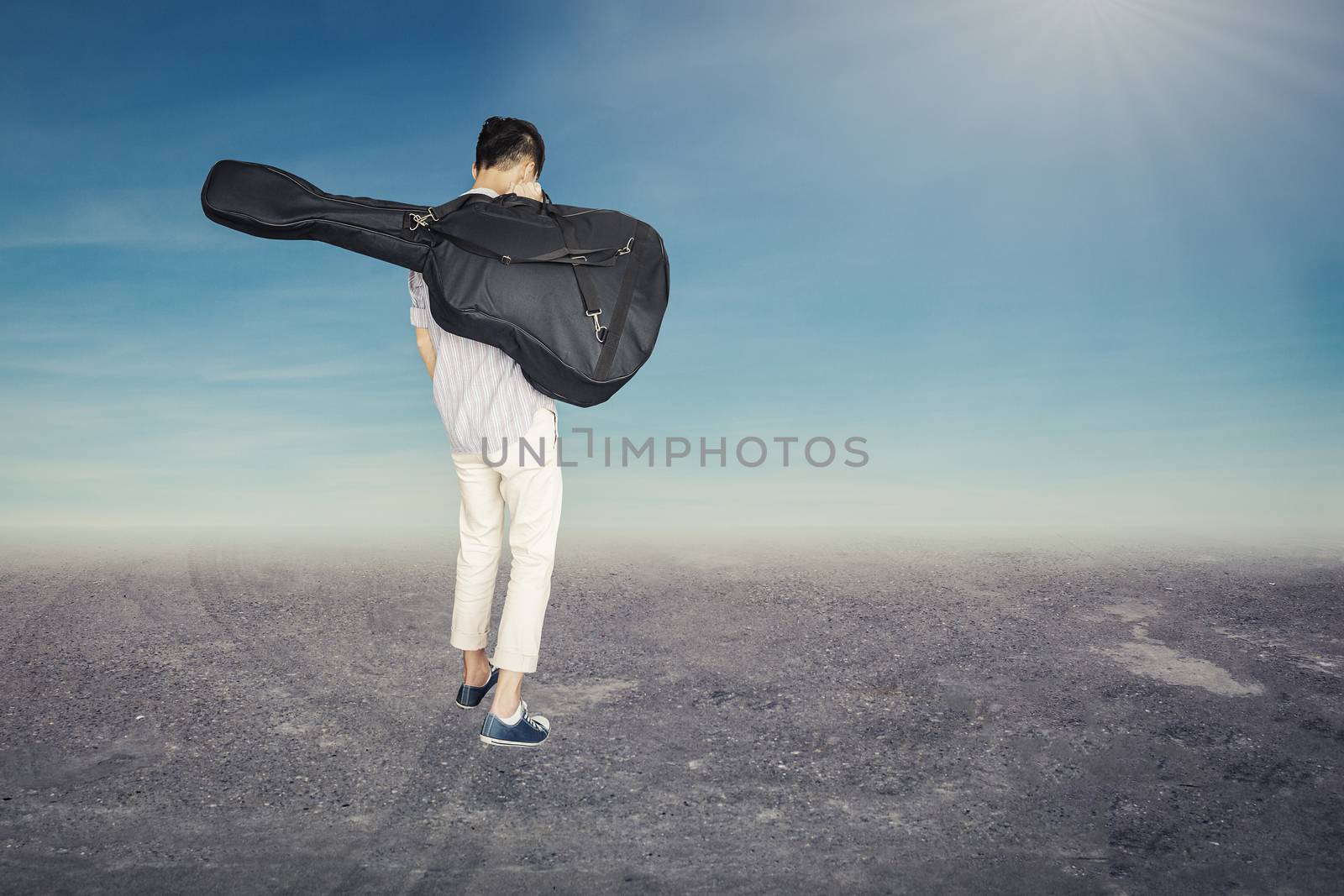 stylish young asian hipster man wear scott strip shirt, and sneaker and walking, hold guitar bag, for concert travelling concept and blue sky background