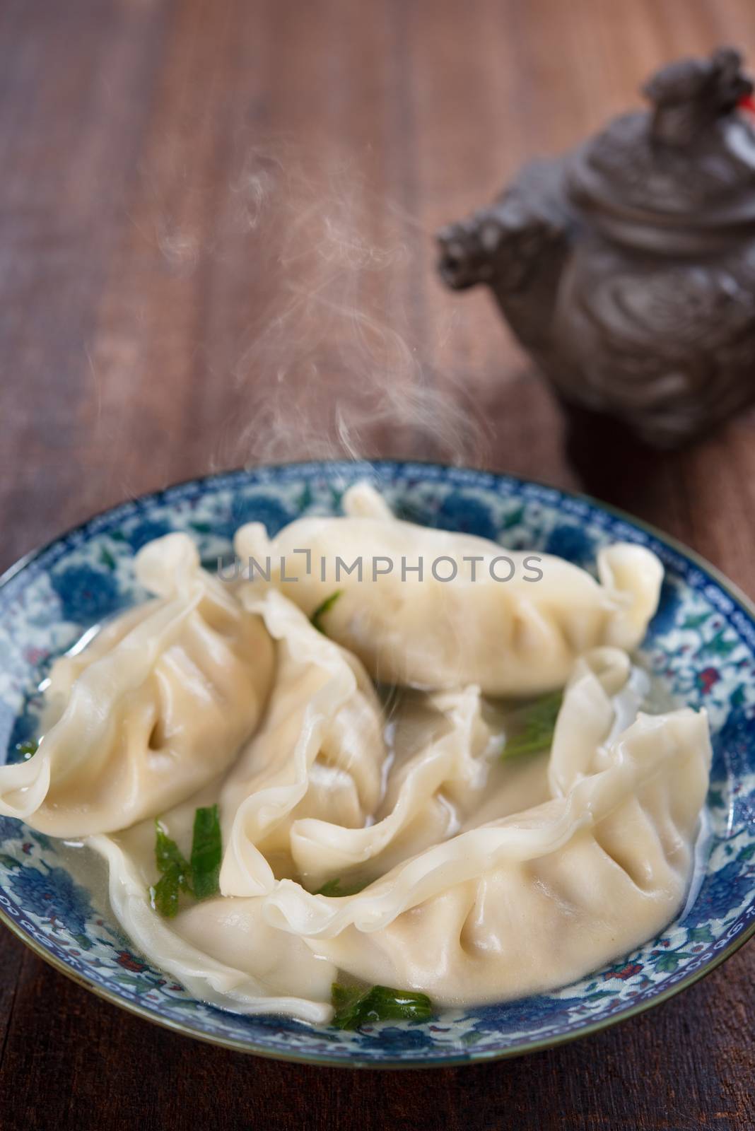 Fresh dumplings soup on plate with hot steams. Chinese cuisine on old vintage wooden background.