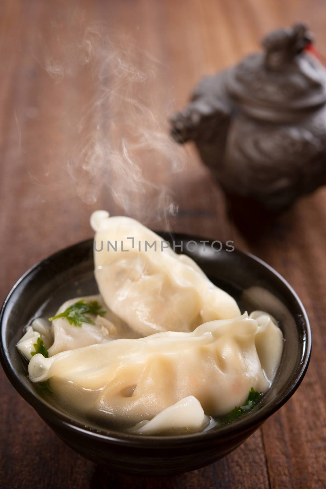 Fresh dumplings soup on plate with hot steams. Chinese dish on rustic old vintage wooden background.