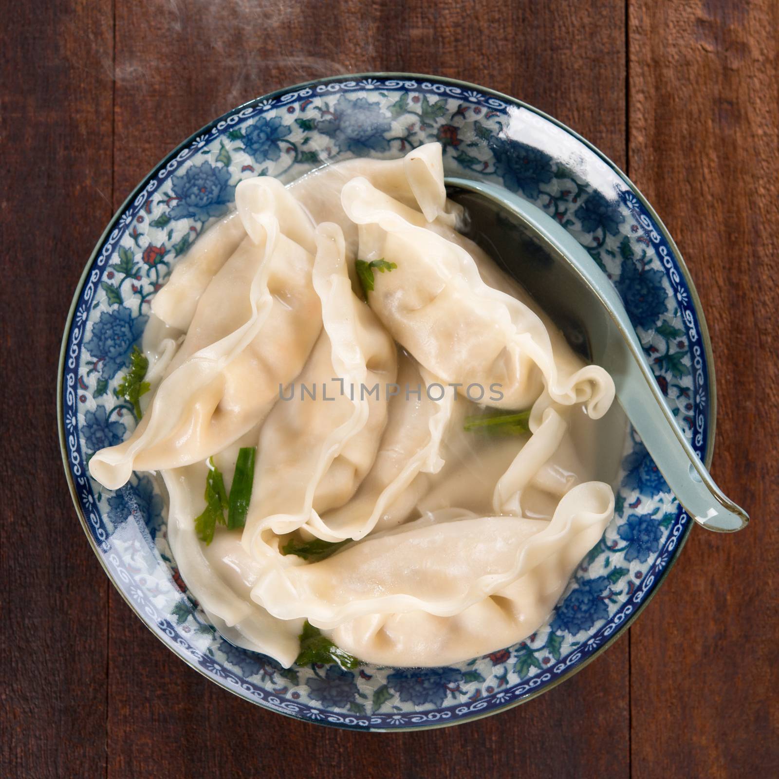 Top view fresh dumplings soup on plate with hot steams. Chinese cuisine on rustic old vintage wooden background.