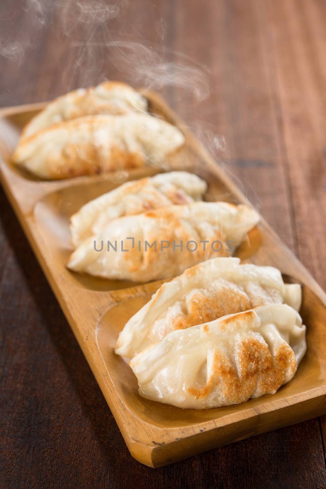 Fresh pan fried dumplings on plate with hot steams. Asian cuisine on rustic old vintage wooden background.