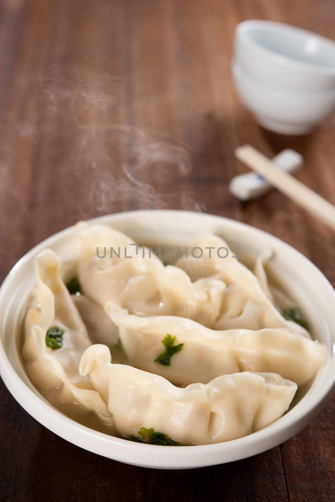 Fresh dumplings soup on plate with hot steams. Chinese meal on old vintage wooden background.
