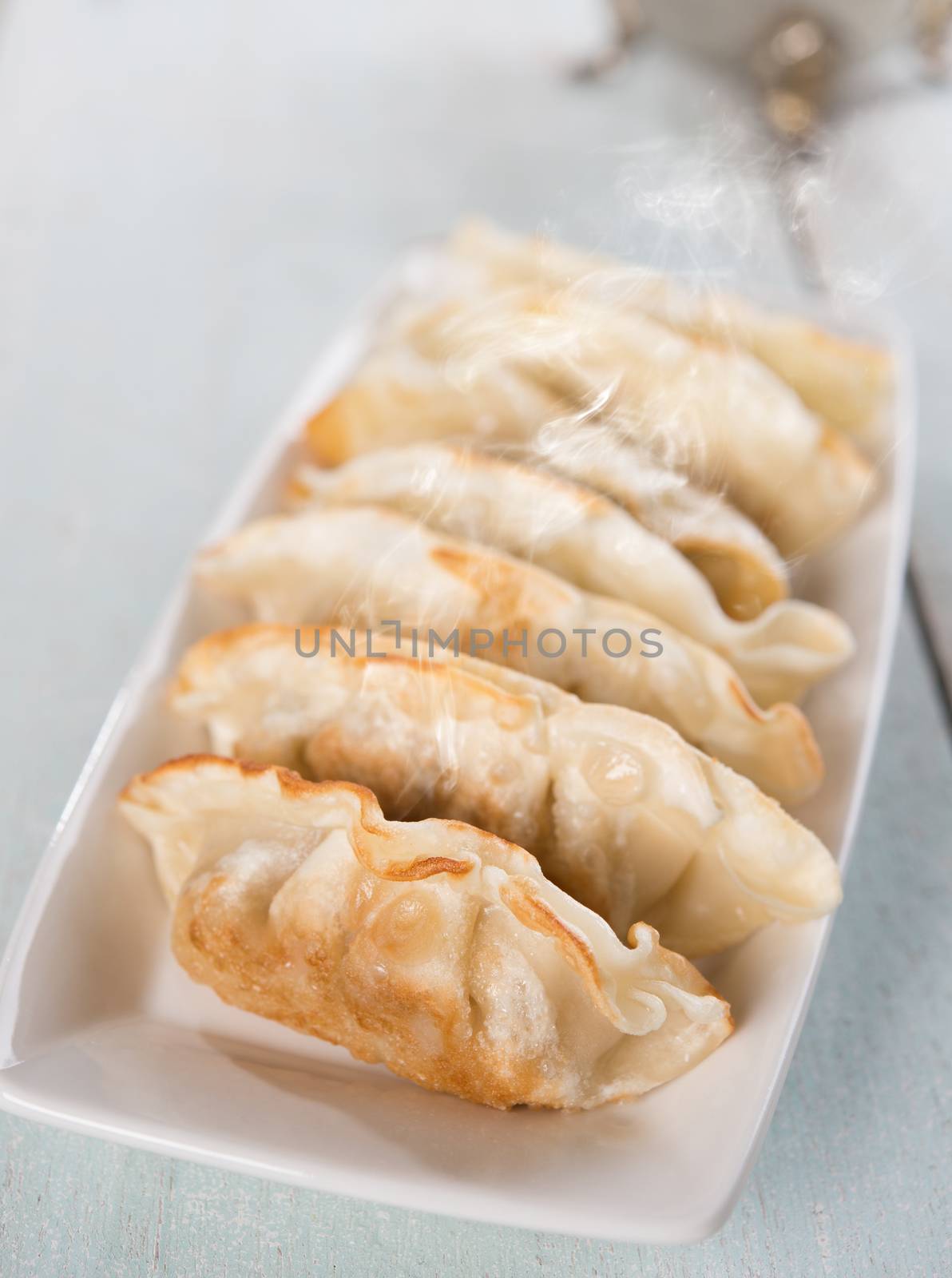 Fresh pan fried dumplings on plate with hot steams. Asian dish on rustic vintage wooden background.