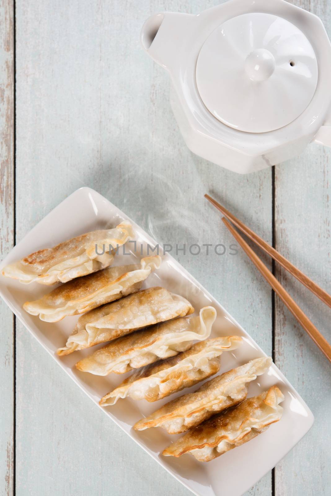 Top view fresh pan fried dumplings on plate with hot steams. Asian cuisine on rustic vintage wooden background.