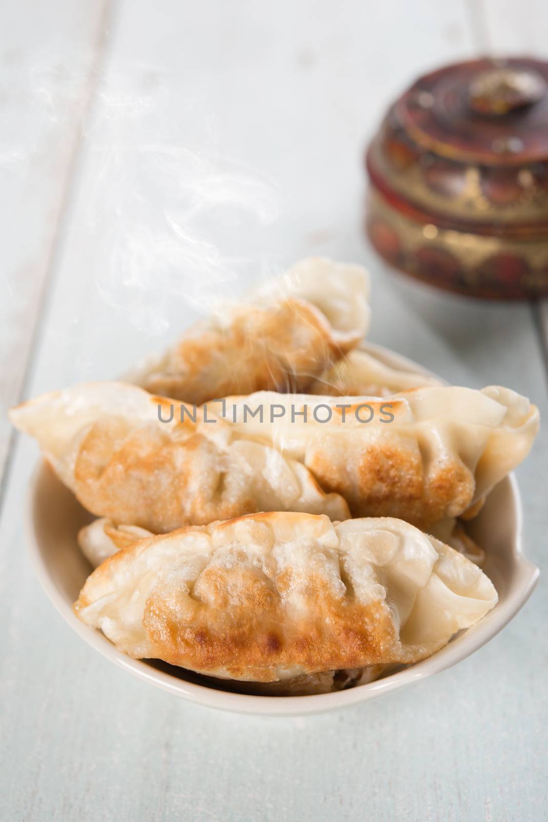 Fresh pan fried dumplings on plate with hot steams. Asian food on rustic vintage wooden background.