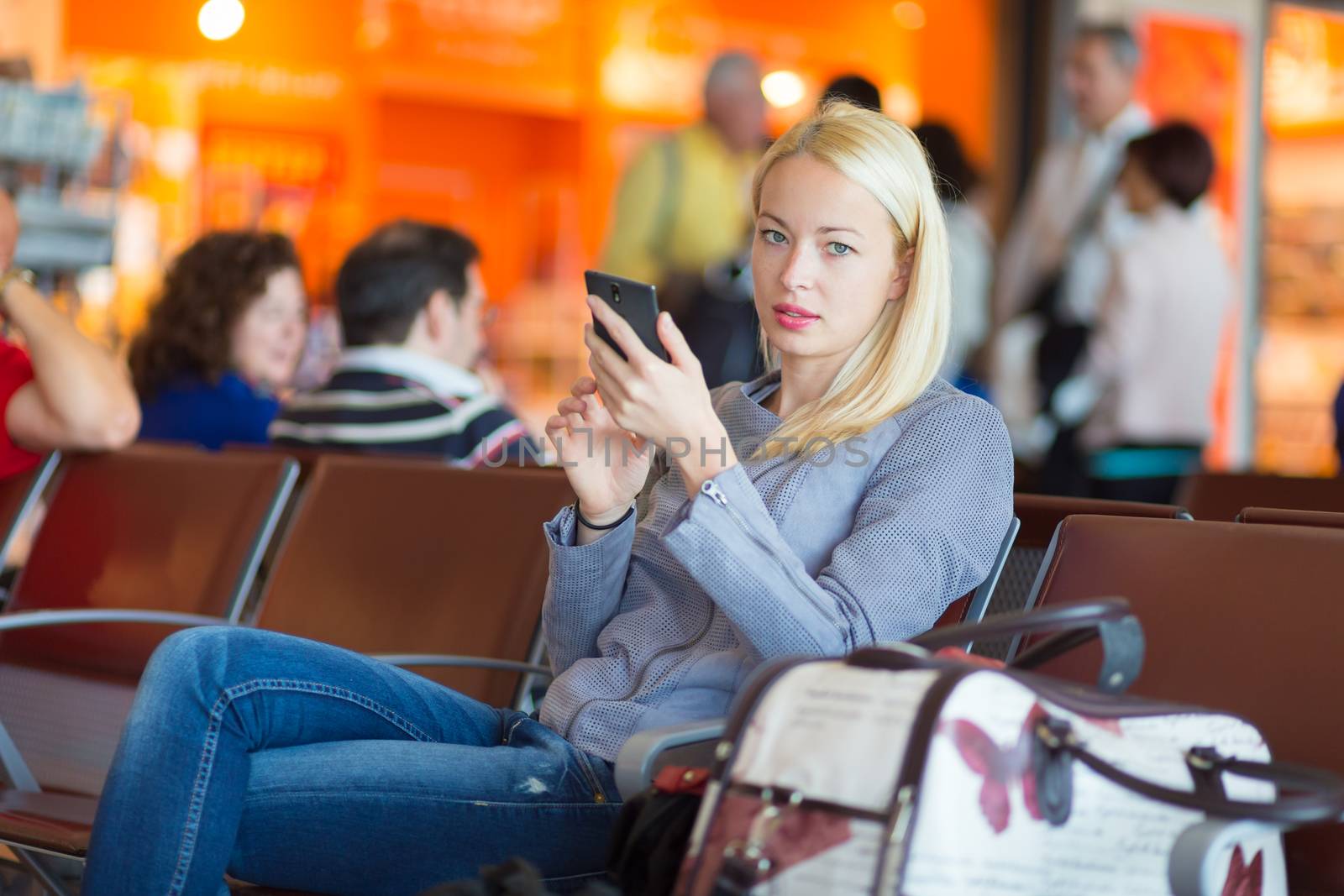 Casual blond young woman using her cell phone while waiting to board a plane at the departure gates. Wireless network hotspot enabling people to access internet conection. Public transport.