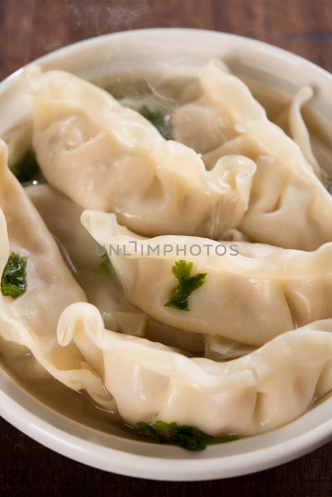 Close up fresh dumplings soup on plate with hot steams. Chinese food on old vintage wooden background.