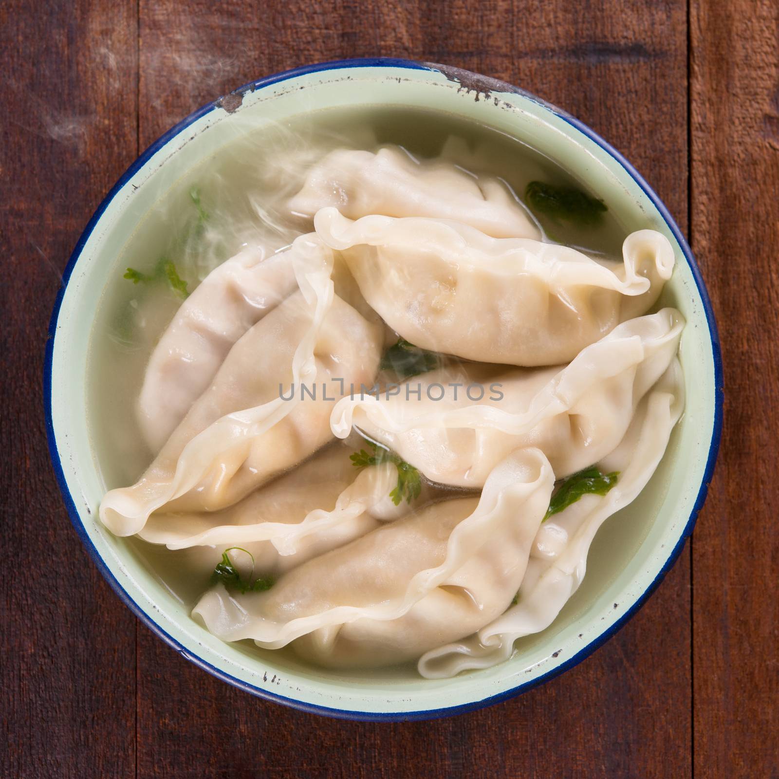 Top view fresh dumplings soup on plate with hot steams. Chinese gourmet on rustic old vintage wooden background.