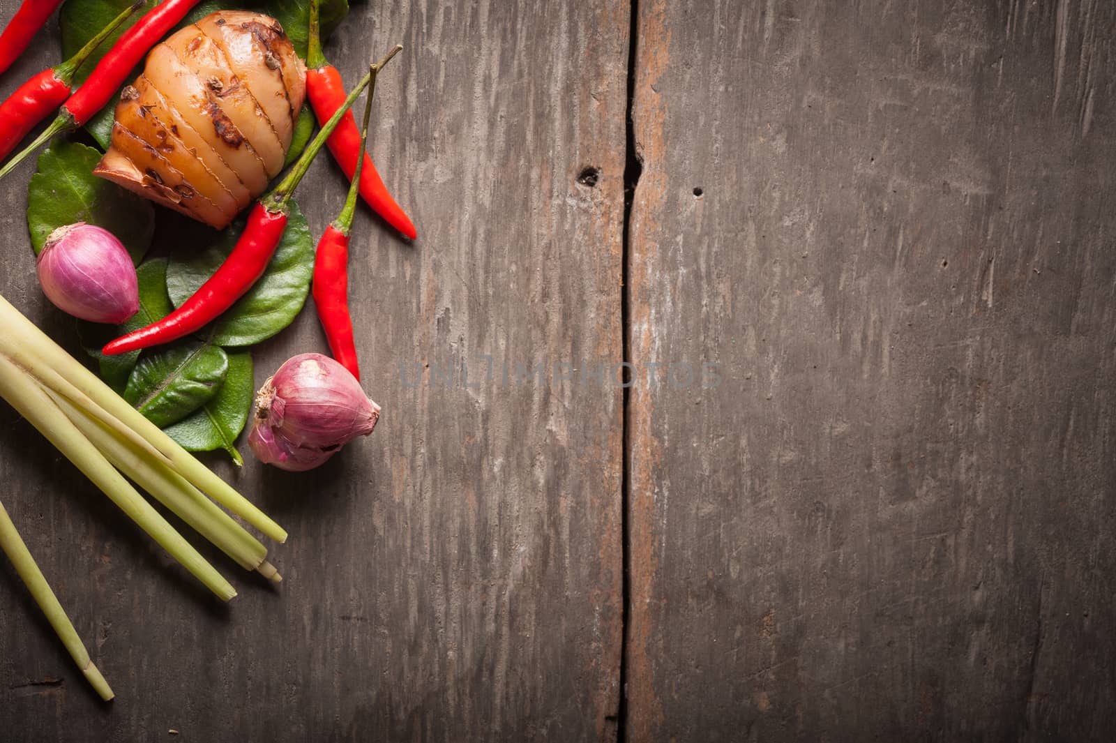 Ingredients set for Thai spicy soup (Tom-yum) include lemon, galangal, red chili, red onion, lemongrass, and kaffir lime leaf on wood table in morning scene with blank area for text or message