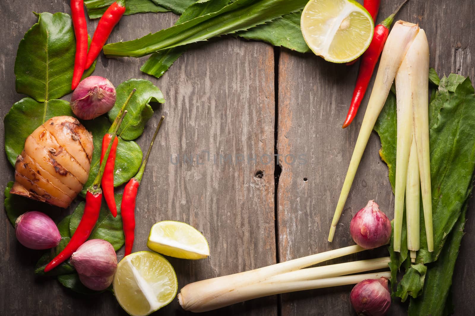 Ingredients set for Thai spicy soup (Tom-yum) include lemon, galangal, red chili, red onion, lemongrass, and kaffir lime leaf on wood table in morning scene with blank area for text or message