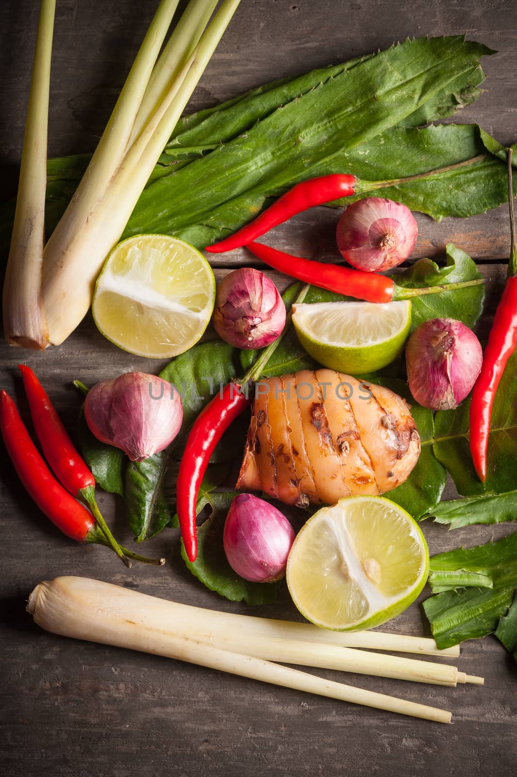 Ingredients set for Thai spicy soup (Tom-yum) include lemon, galangal, red chili, red onion, lemongrass, and kaffir lime leaf on wood table in morning scene
