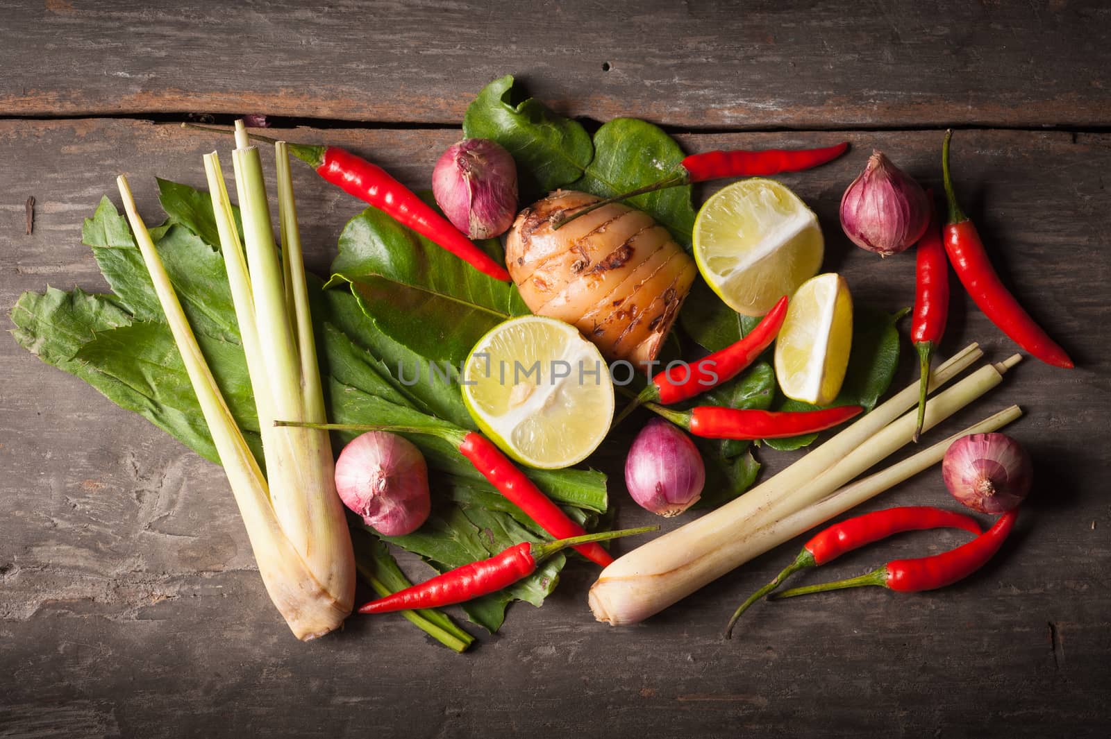 Ingredients set for Thai spicy soup (Tom-yum) include lemon, galangal, red chili, red onion, lemongrass, and kaffir lime leaf on wood table in morning scene