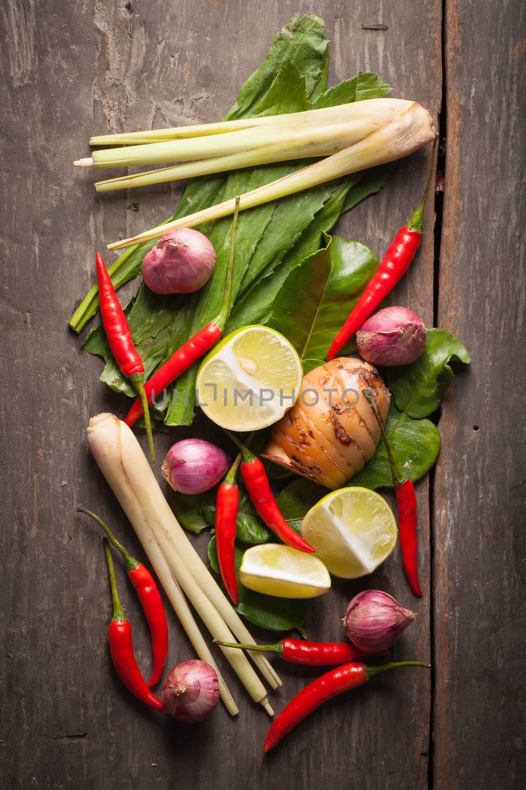 Ingredients set for Thai spicy soup (Tom-yum) include lemon, galangal, red chili, red onion, lemongrass, and kaffir lime leaf on wood table in morning scene