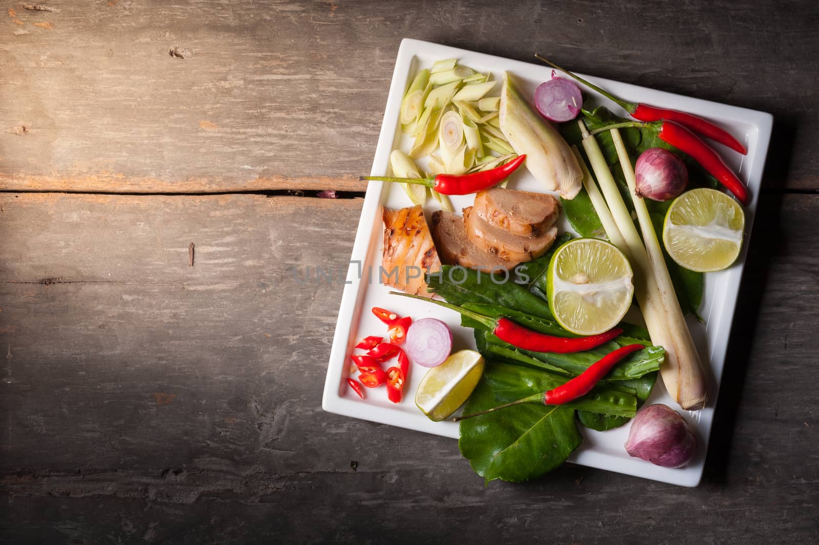 Ingredients set for Thai spicy soup (Tom-yum) include lemon, galangal, red chili, red onion, lemongrass, and kaffir lime leaf on wood table in morning scene with blank area for text or message